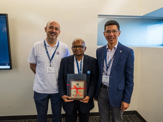 three people standing, person in center holding award