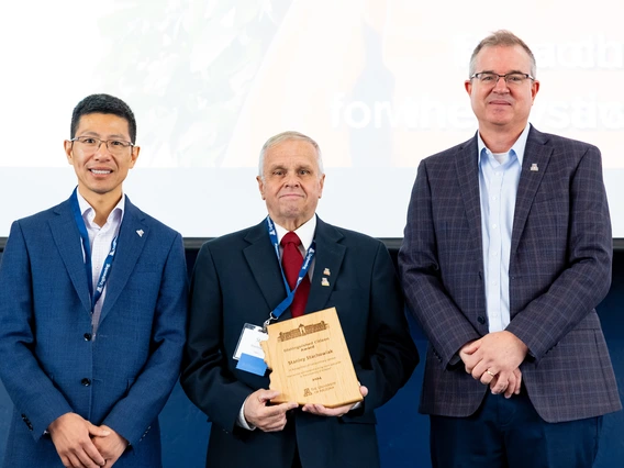 three people standing, person in middle holding an award