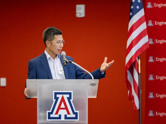 A man in a blue suits peaks on a glass podium.
