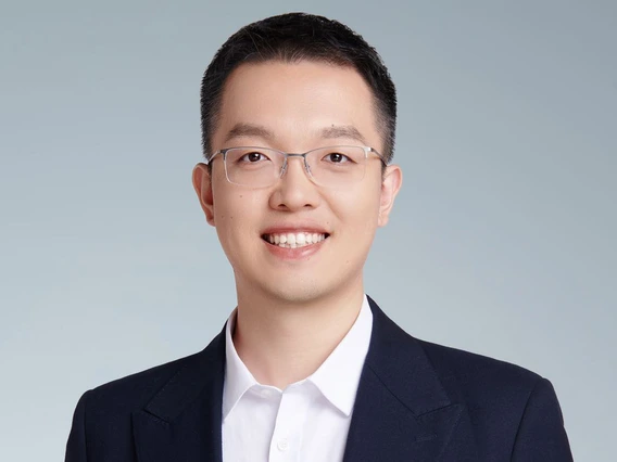 a man in a blue suit stands in front of a grey background.