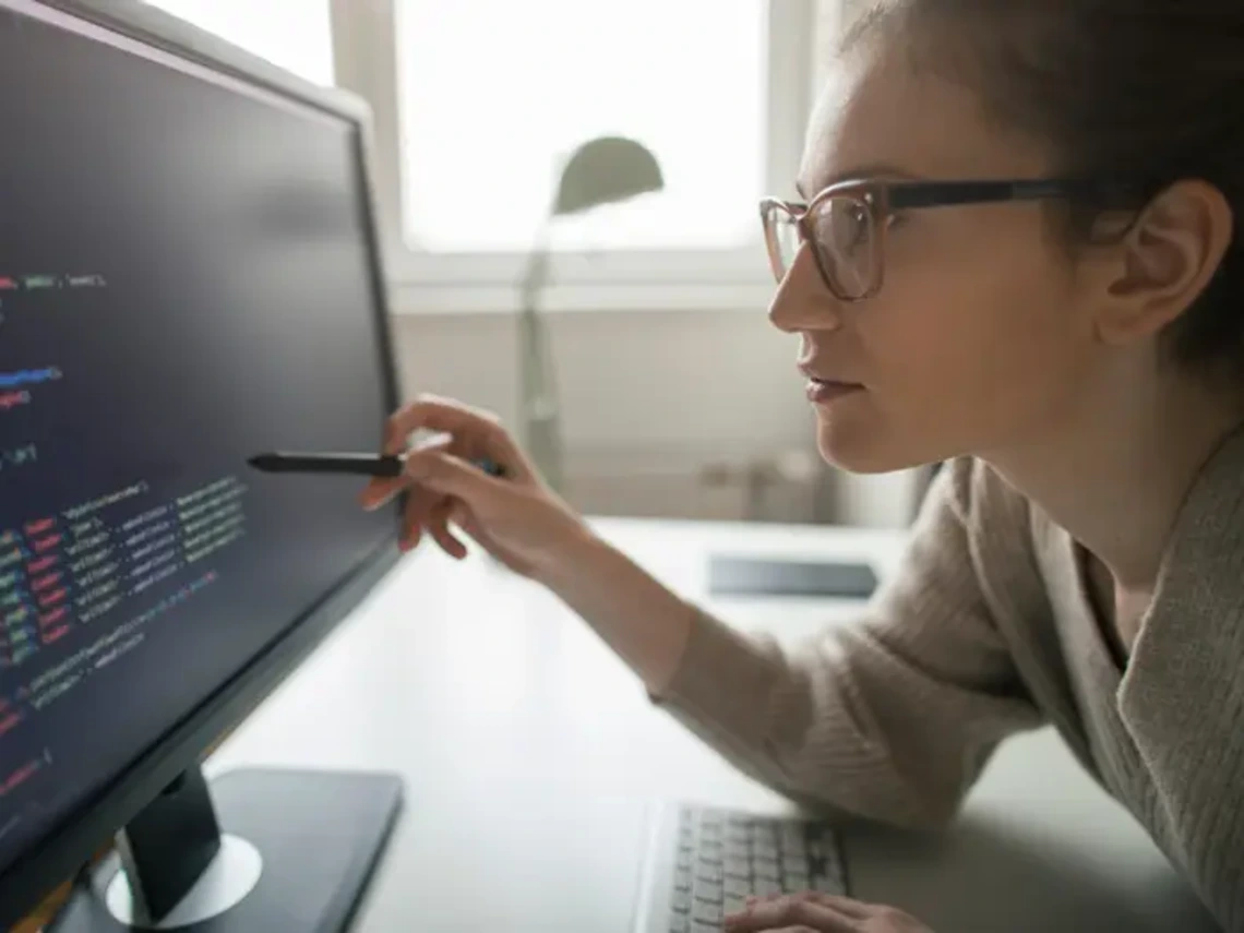 Woman examines code on a computer screen.