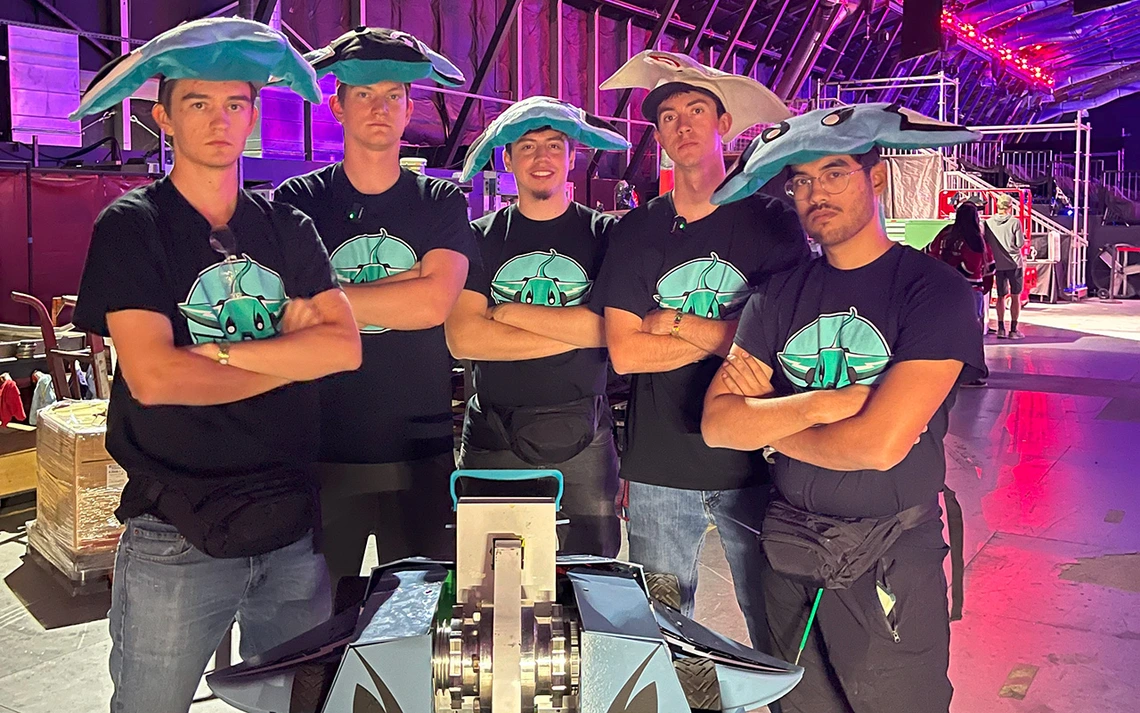 Five men in black t shirts pose for a photo with a robot.