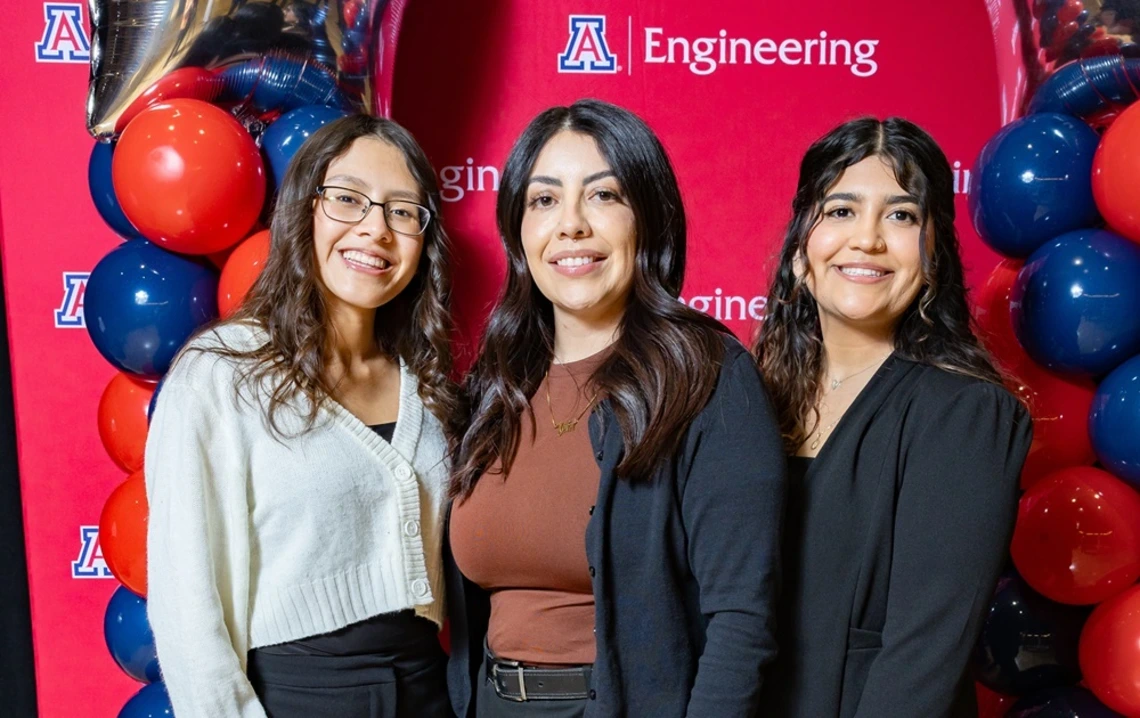 Three people standing in front of Univ of AZ Engineering backdrop with balloons