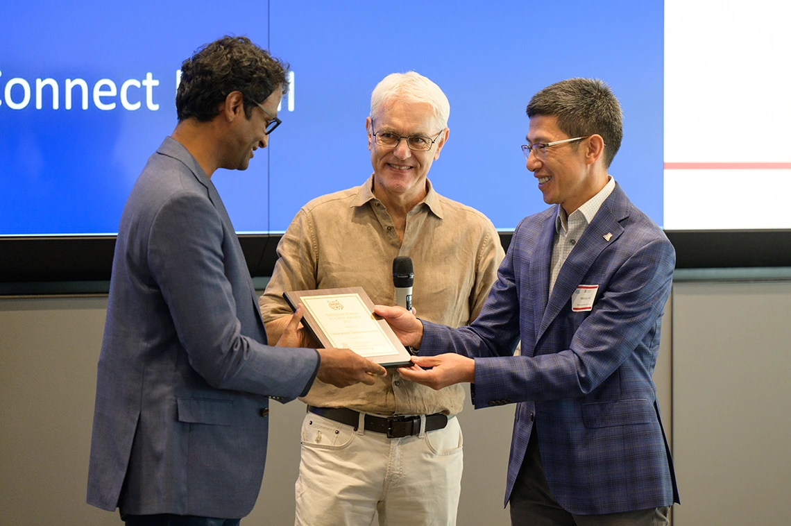 three people standing, one receiving an award