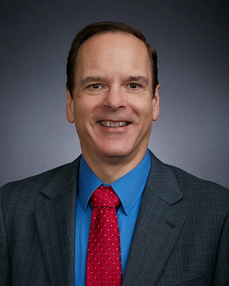 photo of man, smiling, wearing gray suit, blue shirt and red tie