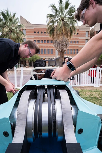 people working on a robot, palm trees in background