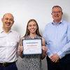 One woman and two men pose for a photo. The woman holds an award certificate.