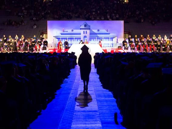 sillouette of graduate walking down aisle, Old Main in background