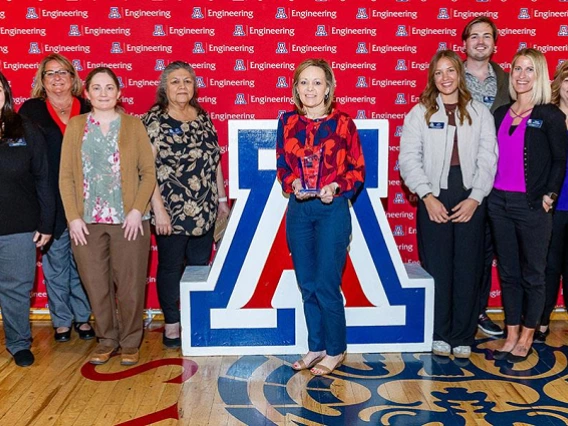 group of people standing by Univ. of Arizona block A. Woman holding award