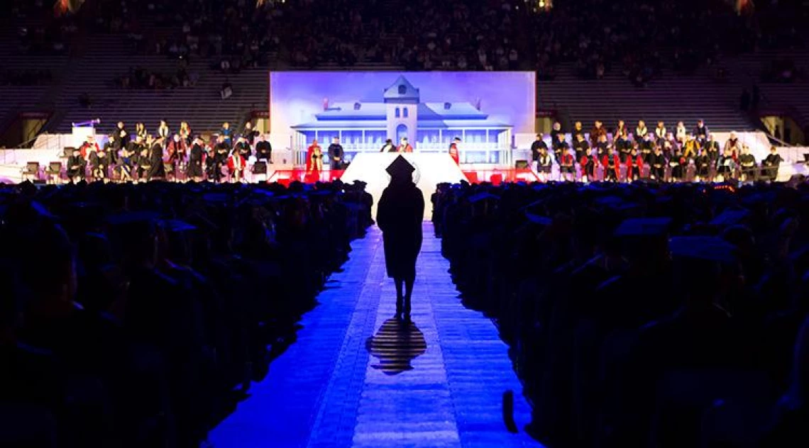 sillouette of graduate walking down aisle, Old Main in background