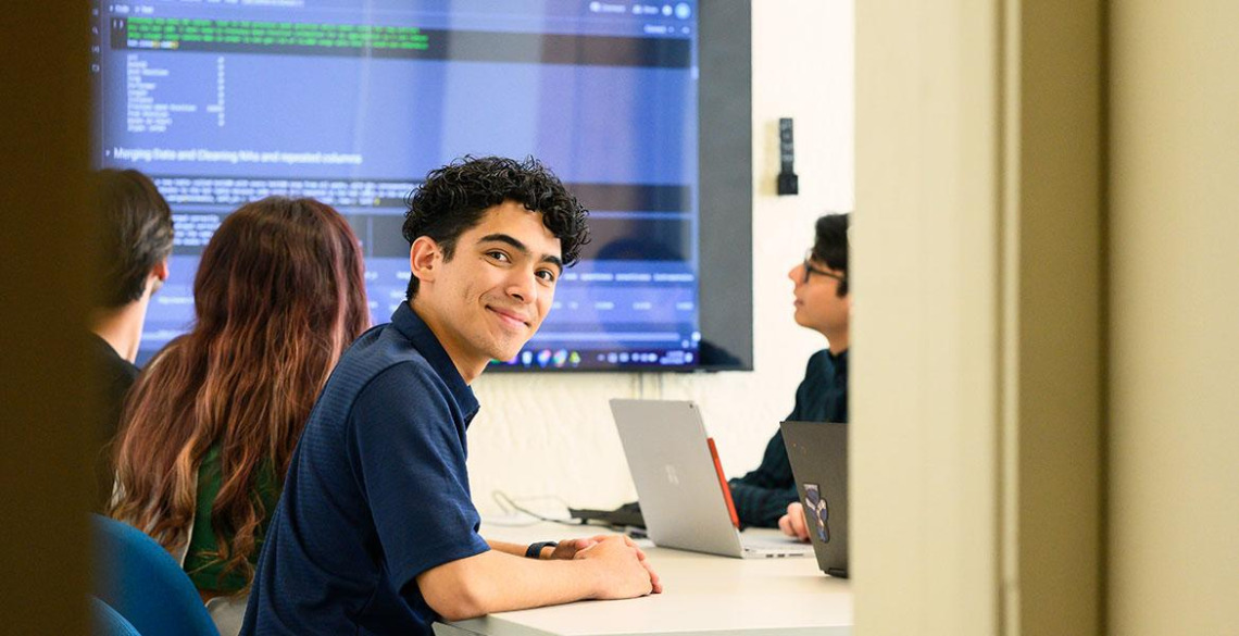 person, smiling, computer screen and students in background