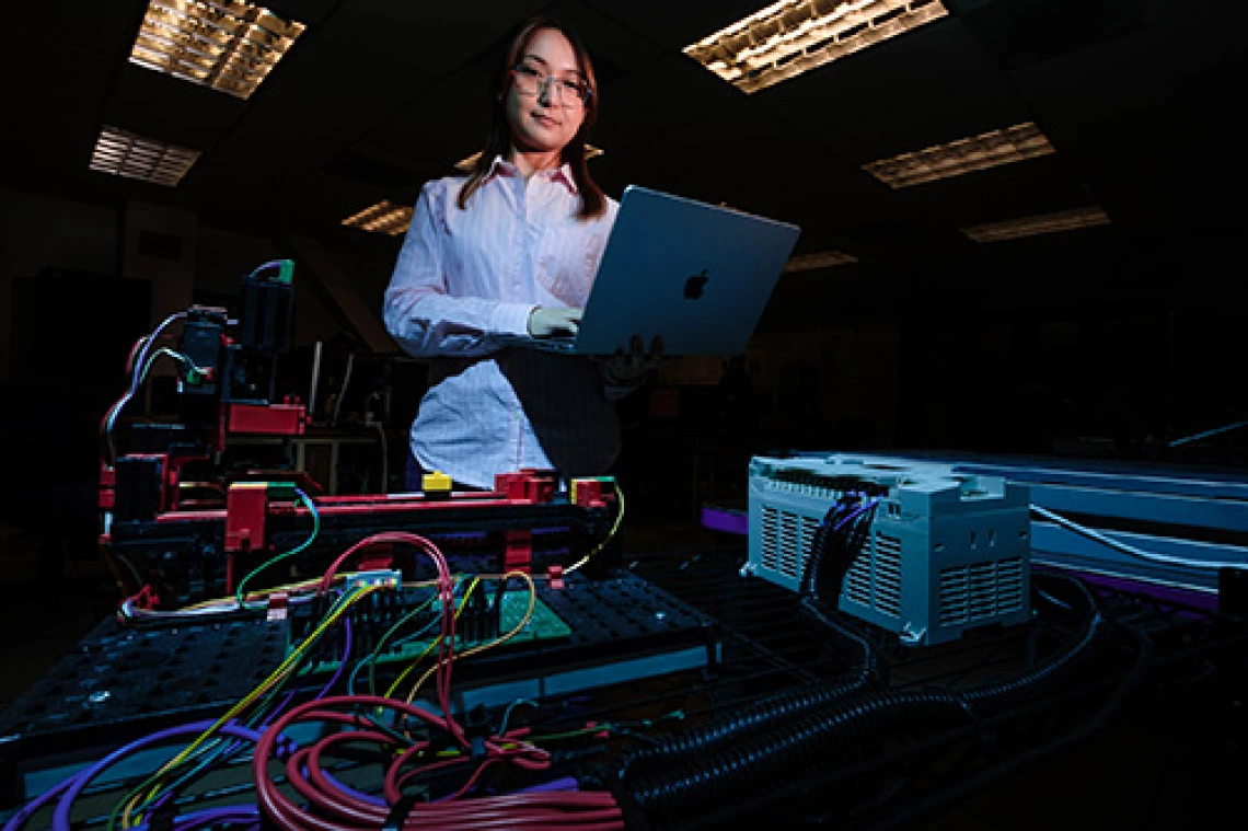 person in lab, wearing glasses, holding computer