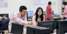 Ming Li and Yanjun Pan, facing the camera, look at a computer monitor in the foreground. Li is pointing at the screen.