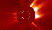 A coronagraph from the Solar and Heliospheric Observatory, showing bright streaks coming out of the center of a red star