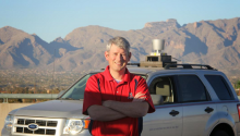 Jonathan Sprinkle standing in front of an autonomous vehicle. Tucson mountains are in the background.