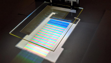 A solar cell -- a silver rectangle reflecting a rainbow of color, sits beneath a rectangular pane of glass.
