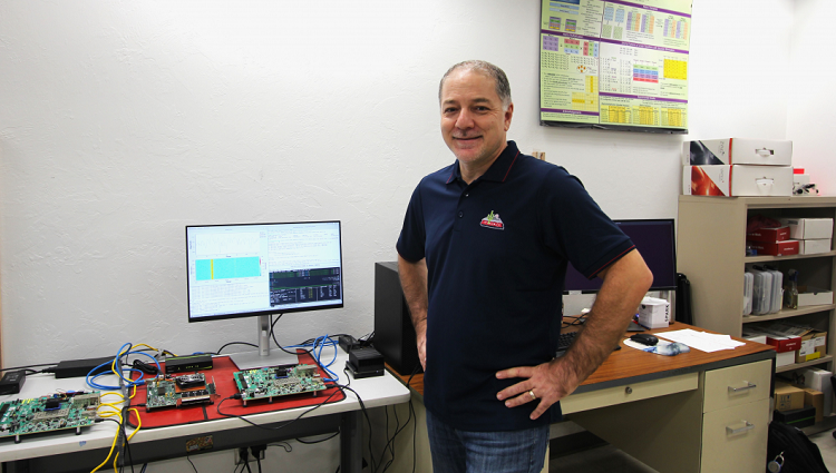 ECE professor Ali Akoglu standing near multiple computers and circuit boards 